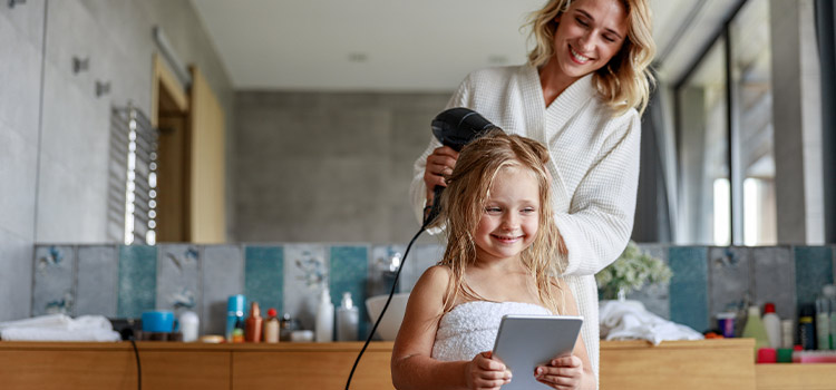 Maman qui sèche les cheveux de sa fille avec un sèche-cheveux