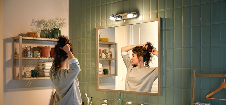 jeune femme qui se coiffe devant son miroir dans une salle de bains